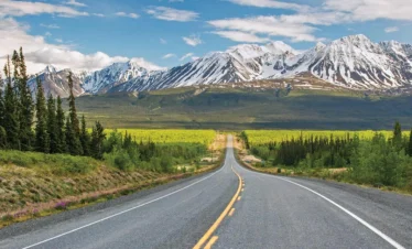 alaska daytime on long straight road with snowy mountains in background