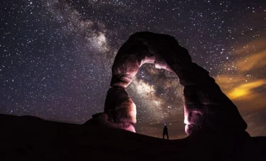 national parks stone formation at night with stars guy standing under rock