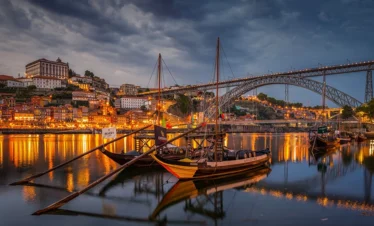 portugal at night with two boats on water overlooking bridge